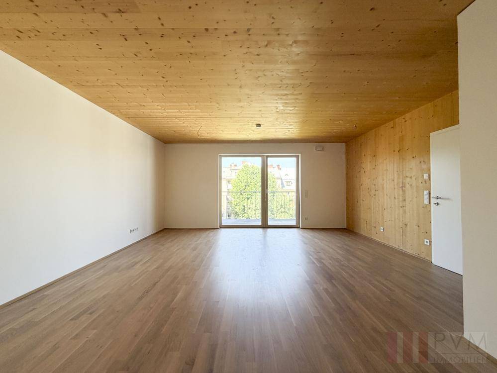 Heller, leerer Wohnraum mit Holzboden, Holzdecke und Zugang zu einem französischen Balkon.