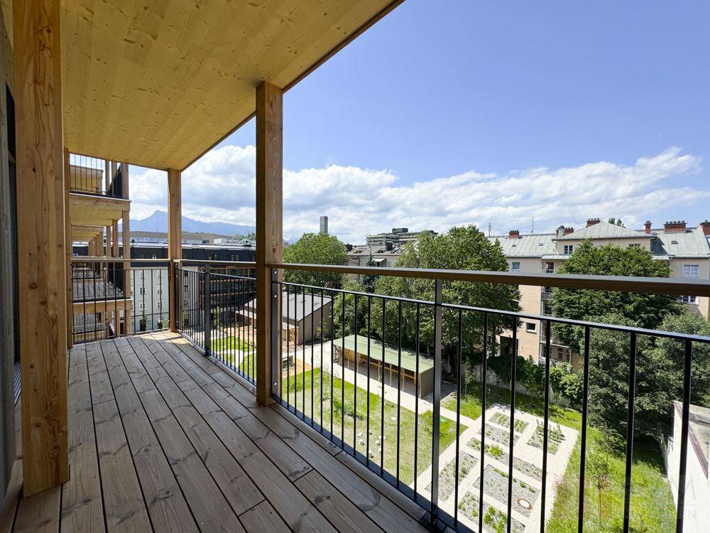 Geräumiger Holzbalkon mit Blick auf den begrünten Innenhof und die umliegende Stadt.