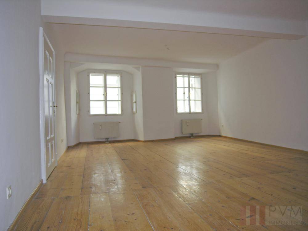 Heller, leerer Raum mit Holzdielenboden und zwei großen Fenstern.