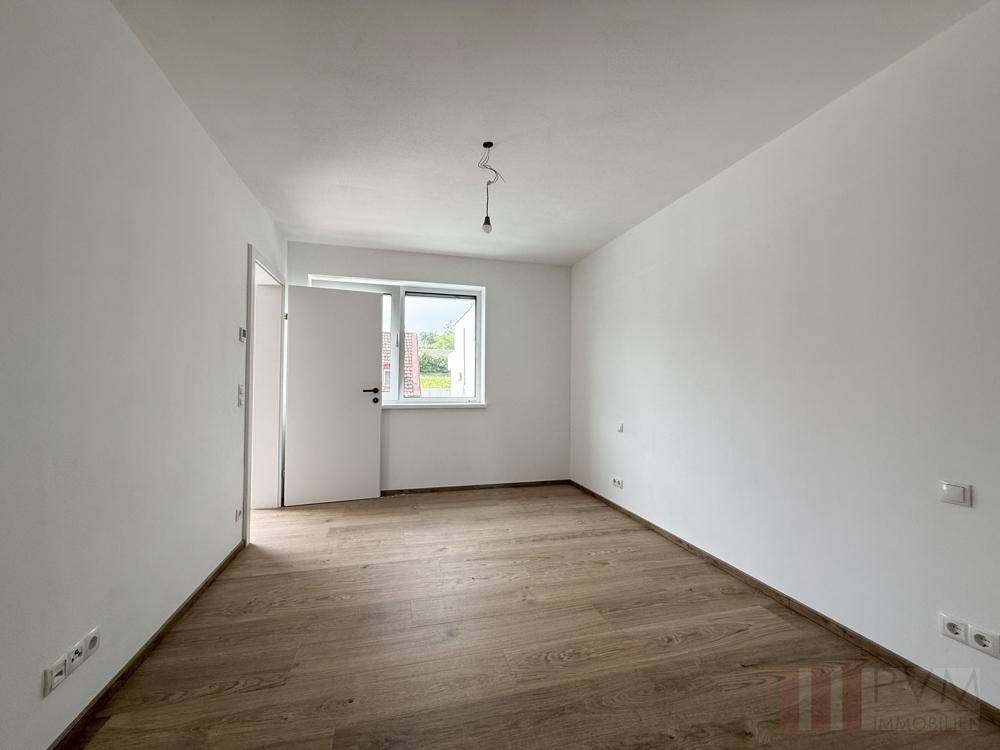 Helles, unmöbliertes Schlafzimmer mit Holzboden und großem Fenster.