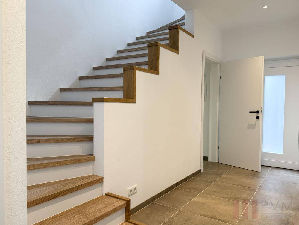 Elegante Holztreppe im Eingangsbereich mit Fliesenboden und heller Gestaltung.