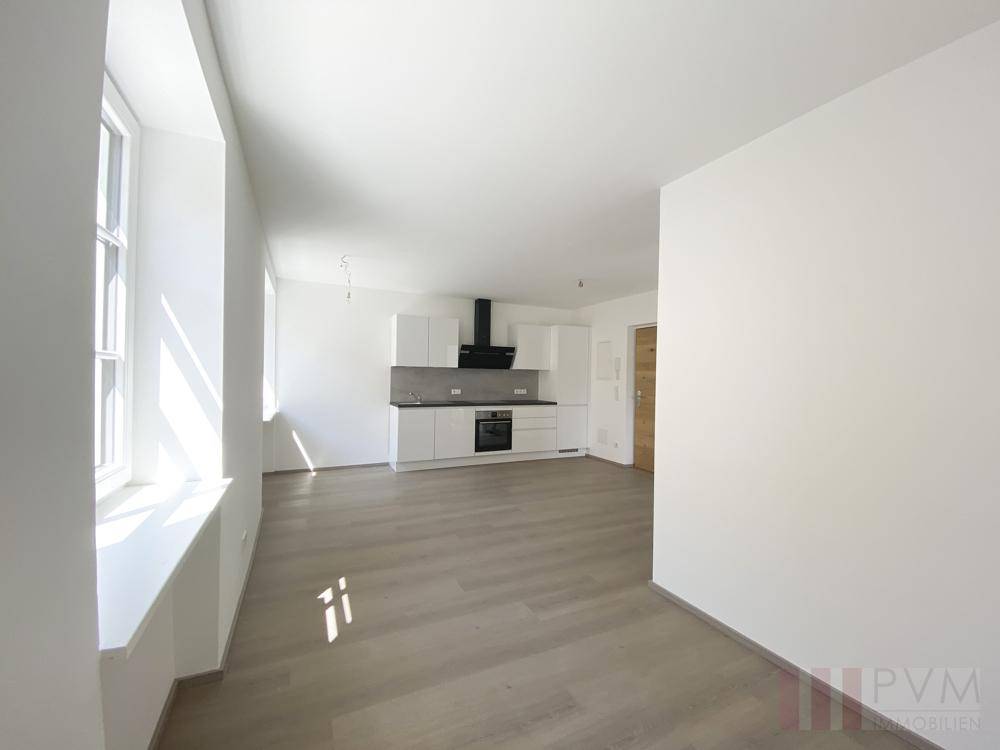 Geräumiger Wohnbereich mit viel Tageslicht und Blick auf die moderne Küchenzeile.
