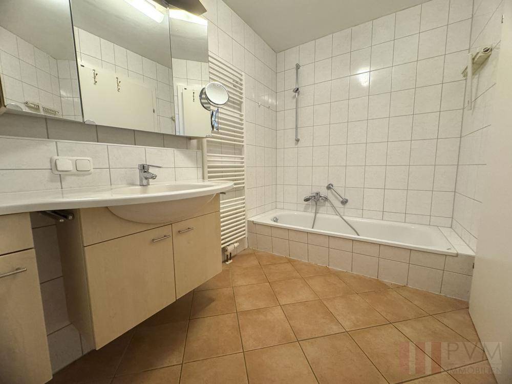 Funktionales Badezimmer mit Fliesenboden, Badewanne, Waschbecken und beheiztem Handtuchhalter.