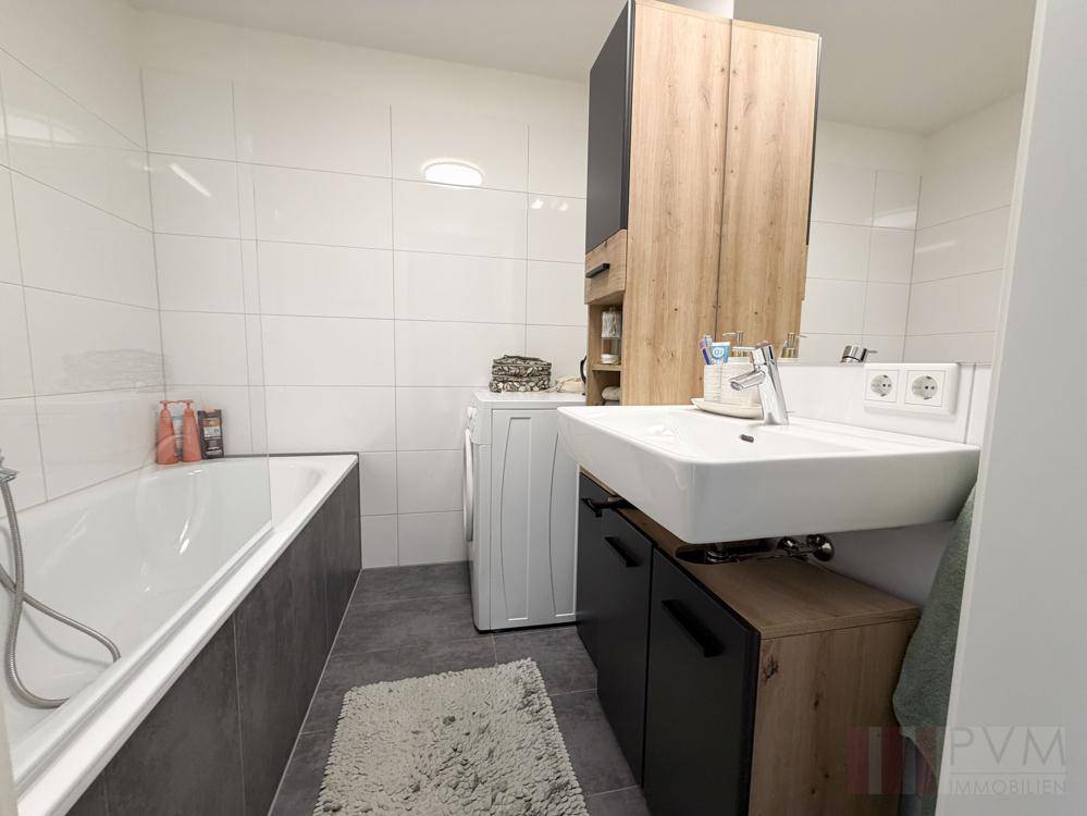Modernes Badezimmer mit Badewanne, Waschbecken und Waschmaschine, hell gefliest.