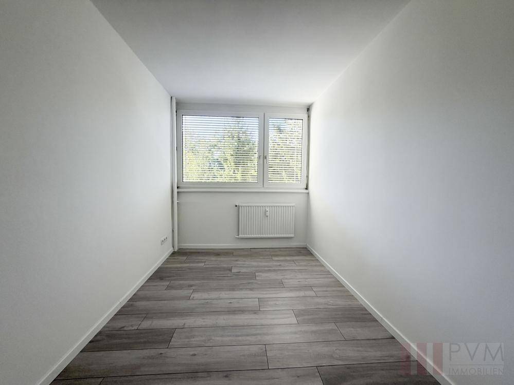 Kleines, helles Zimmer mit Holzoptik-Fliesenboden und Fenster mit Jalousien.