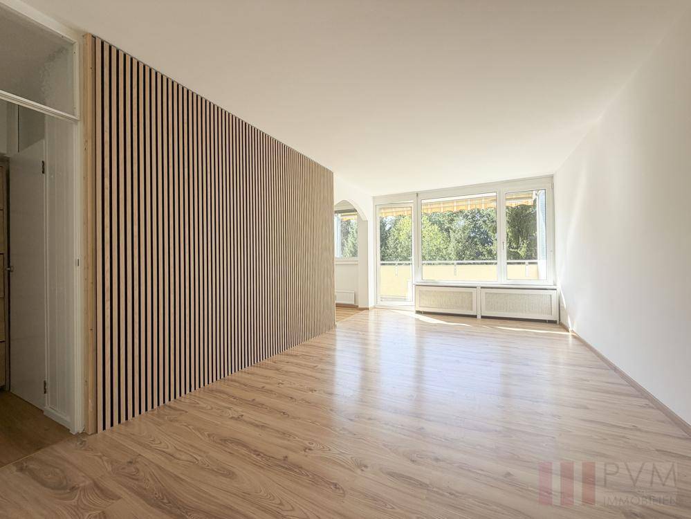 Geräumiges Wohnzimmer mit Holzlaminatboden und einer dekorativen Holzlamellenwand.