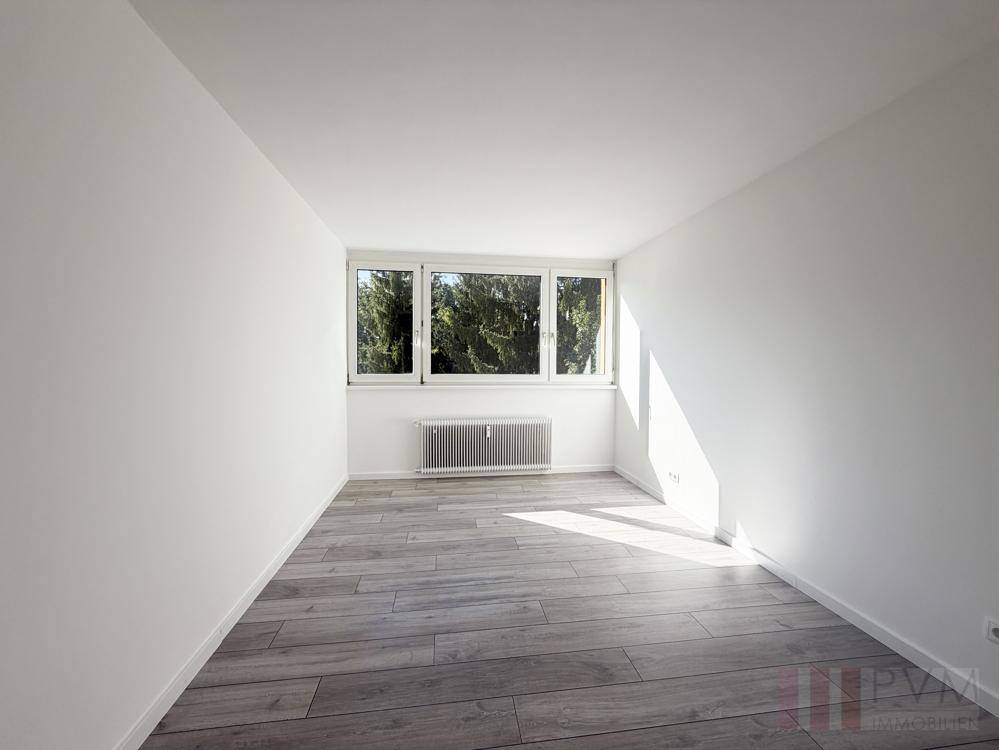 Helles Zimmer mit Holzoptik-Fliesenboden und großem Fenster mit Blick ins Grüne.