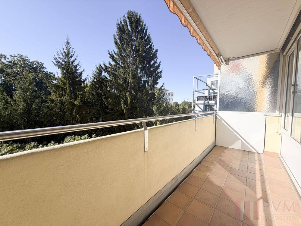Sonniger Balkon mit Fliesenboden und Blick ins Grüne, ausgestattet mit einer Markise.