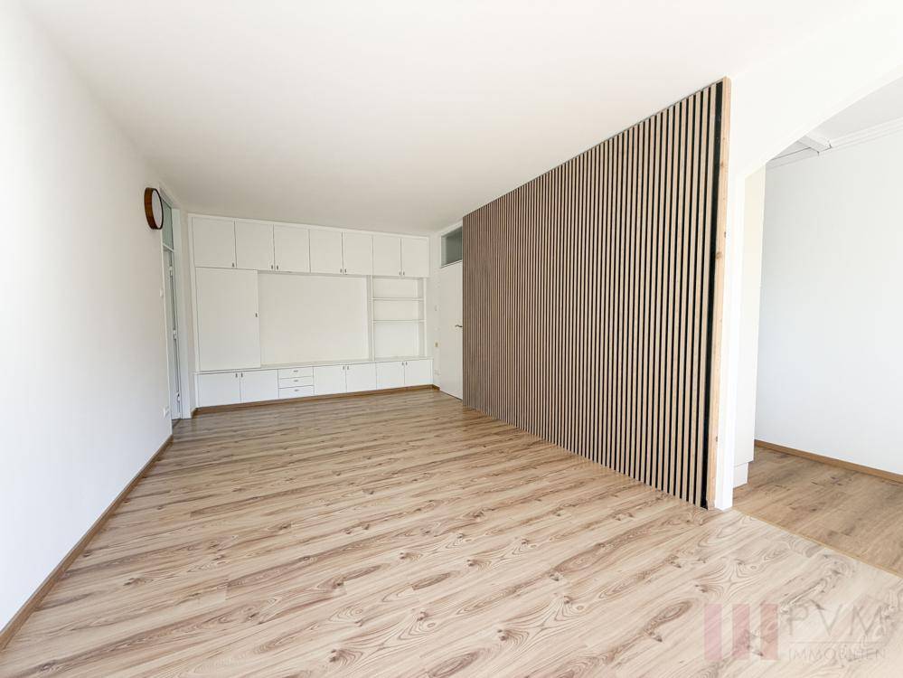 Helles Wohnzimmer mit Laminatboden, Einbauschränken und einer dekorativen Holzlamellenwand.