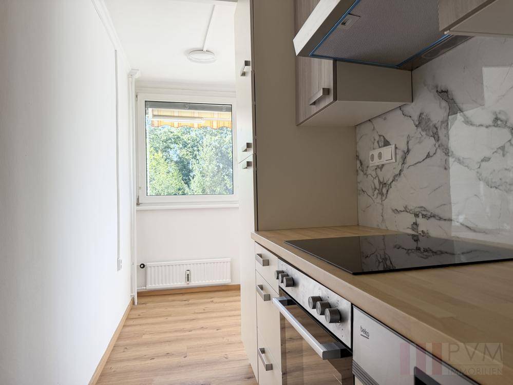 Helle Küche mit Induktionskochfeld, Backofen und Fenster mit Blick ins Grüne.