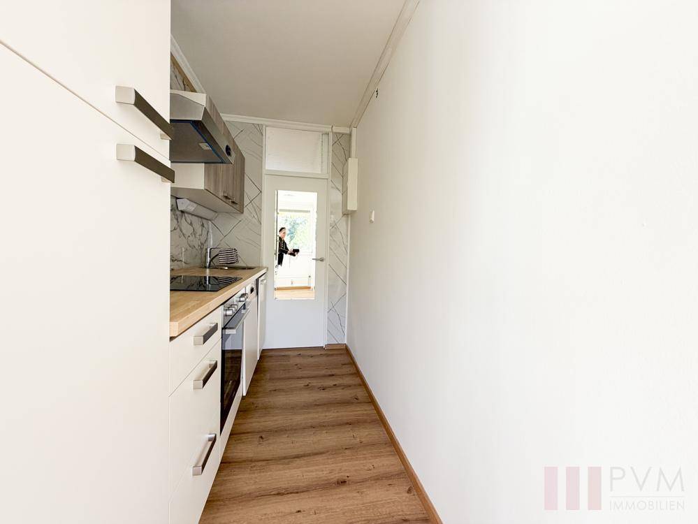 Schmale Küche mit moderner Einbauküche, Holzarbeitsplatte und Laminatboden.