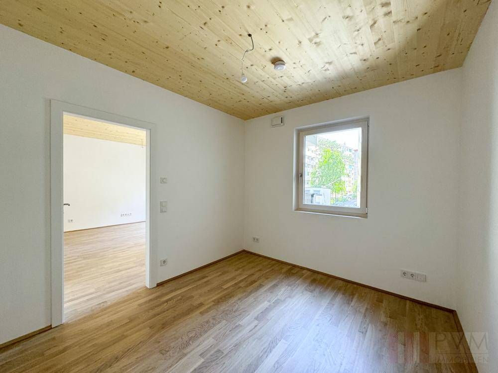 Helles Zimmer mit Holzbalkendecke und einem Fenster, das einen Blick nach draußen bietet.