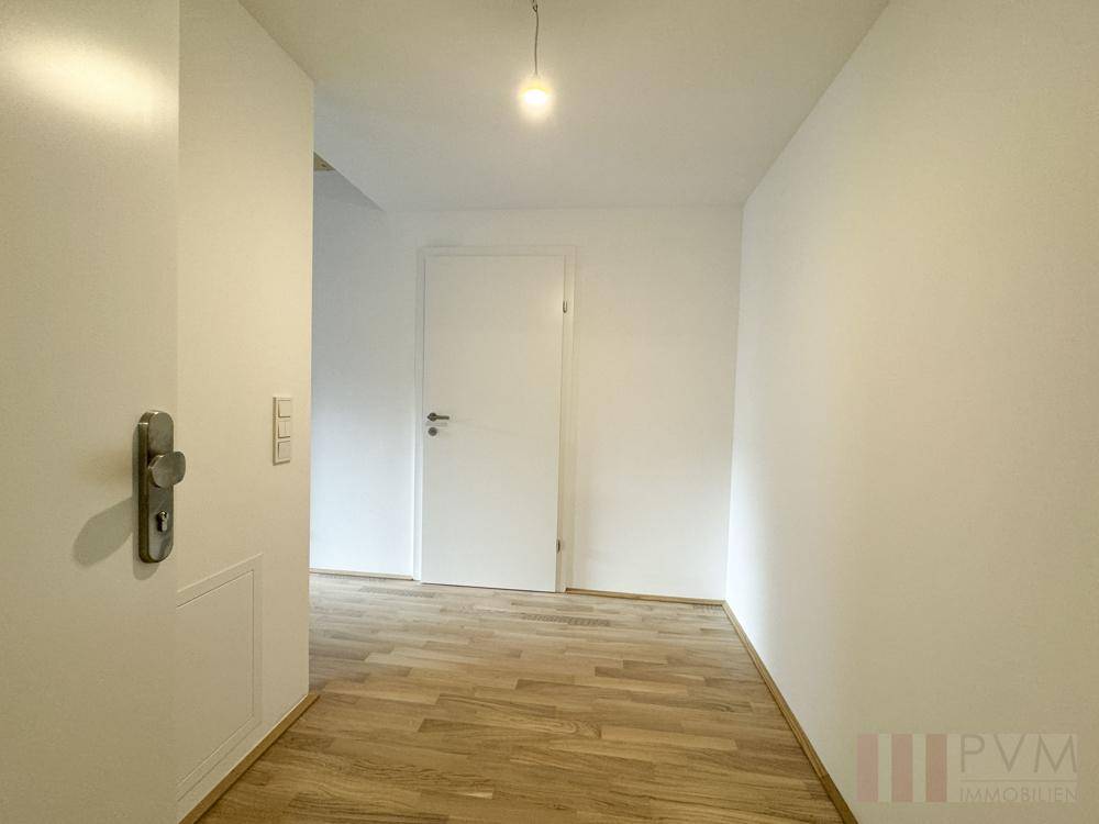 Heller Flur mit Holzboden und weiß gestrichenen Wänden, der zu weiteren Räumen führt.