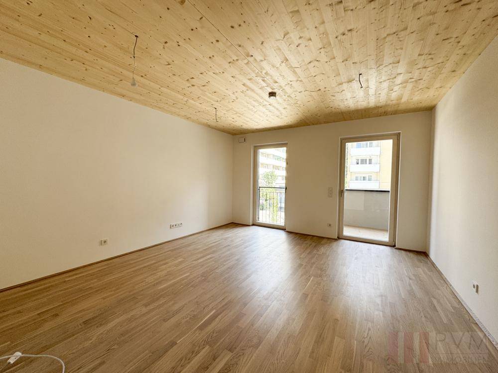 Geräumiges, unmöbliertes Zimmer mit Holzbalkendecke und zwei Balkontüren für viel Licht.