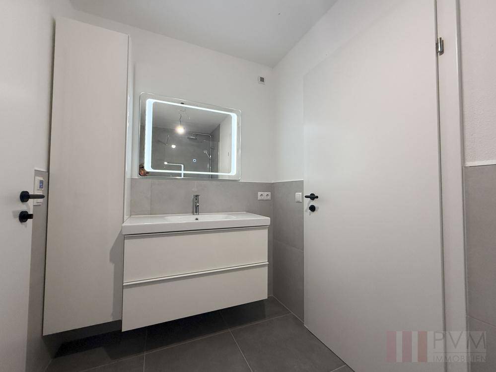Modernes Badezimmer mit Einzelwaschbecken, beleuchtetem Spiegel und weißen Türen.