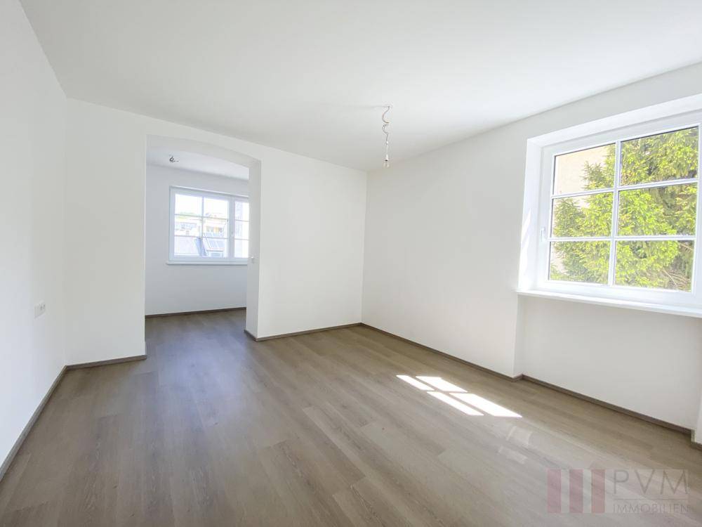 Heller Raum mit Laminatboden und einem Durchgang zu einem weiteren Zimmer.