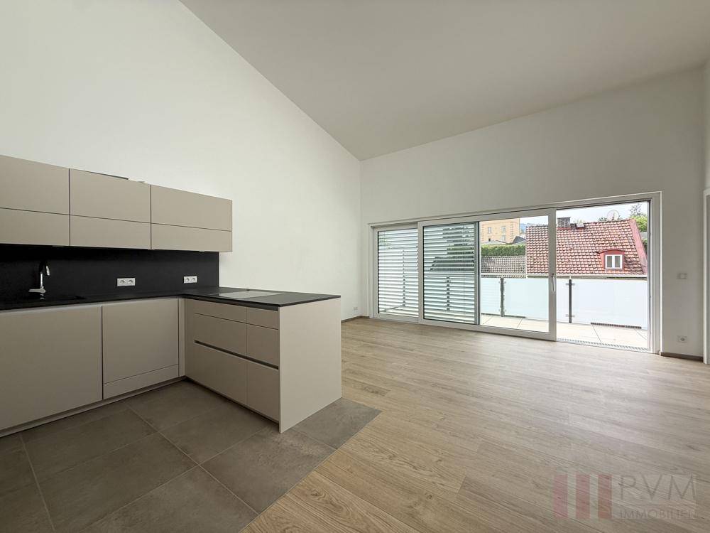 Heller, offener Wohnbereich mit moderner Küche, Holzboden und direktem Zugang zum Balkon.