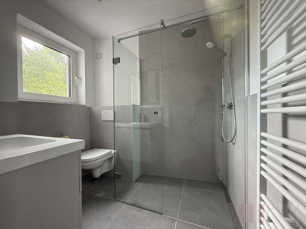 Modernes Badezimmer mit ebenerdiger Dusche, Wand-WC und Fenster für Tageslicht.