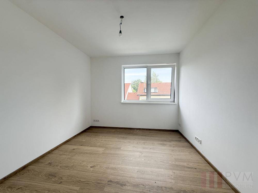 Helles Schlafzimmer mit Holzboden und einem Fenster mit Blick auf die Dächer der Umgebung.