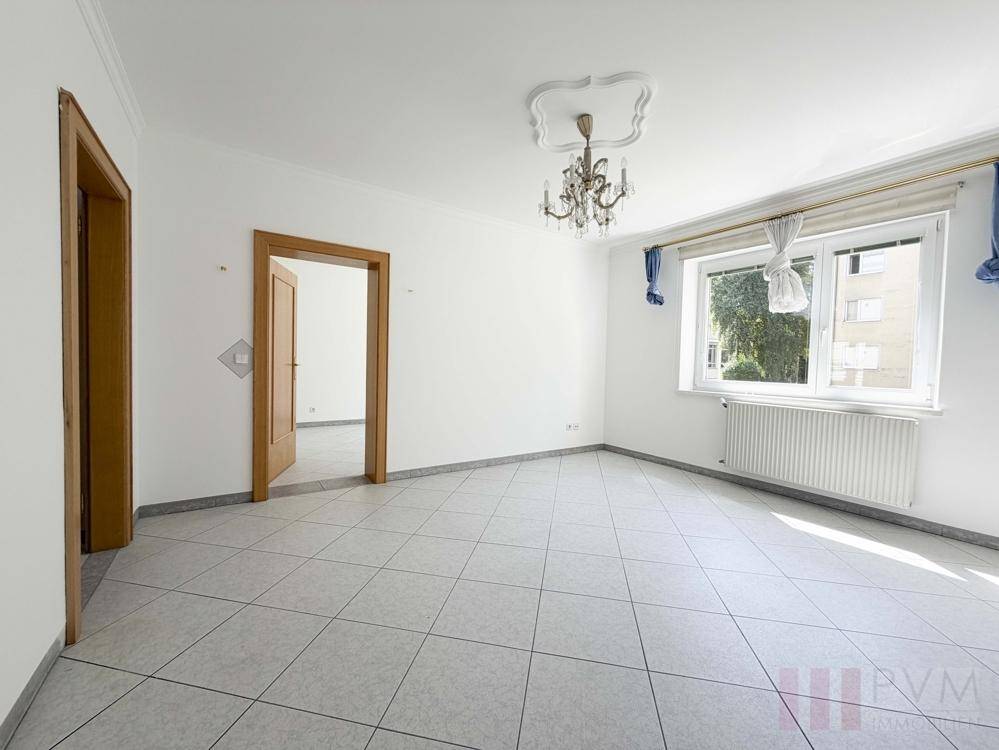 Geräumiges Wohnzimmer mit Fliesenboden, Stuckdecke und Kronleuchter, bereit zur individuellen Gestaltung.