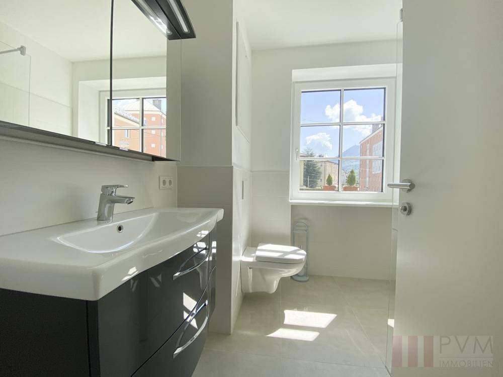 Modernes Badezimmer mit Waschtisch, Spiegelschrank, WC und Fenster für Tageslicht.
