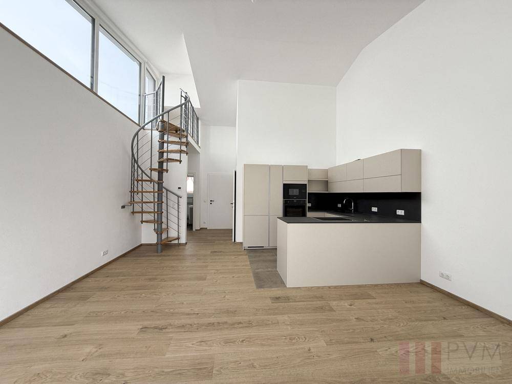 Lichtdurchfluteter Wohnbereich mit offener Küche, Wendeltreppe und hohen Decken.