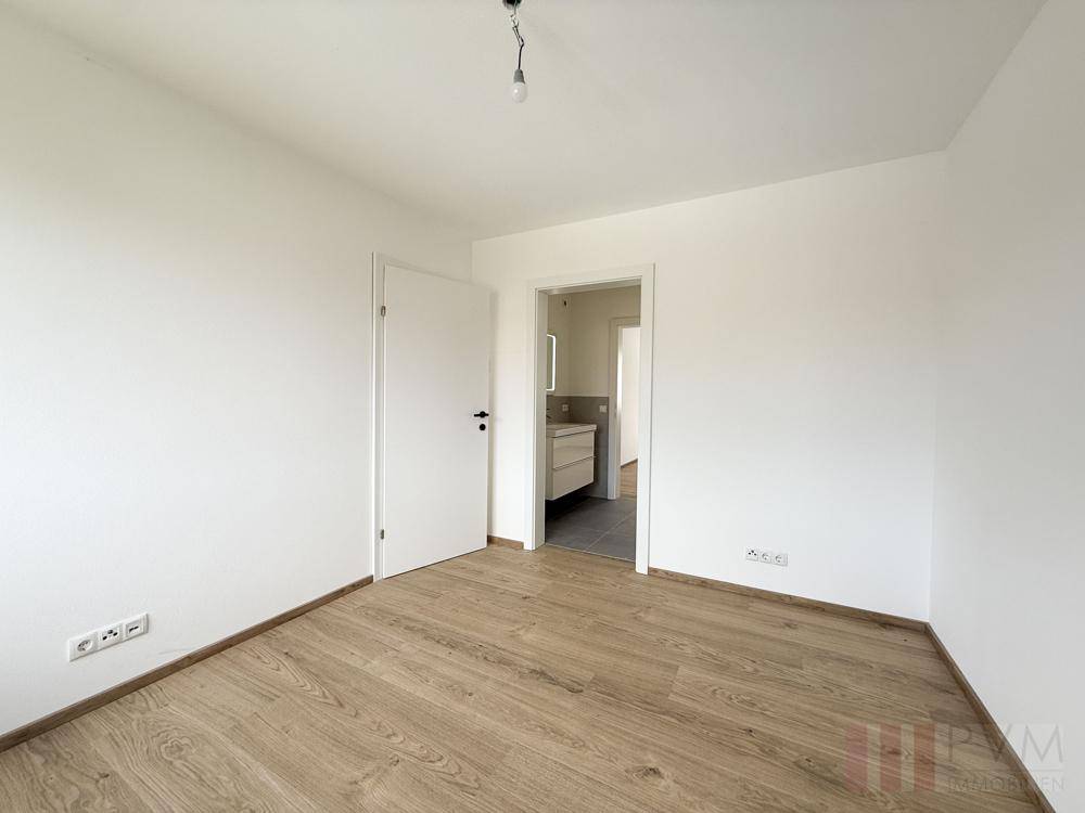 Schlafzimmer mit Holzboden und direktem Zugang zu einem modernen Badezimmer.