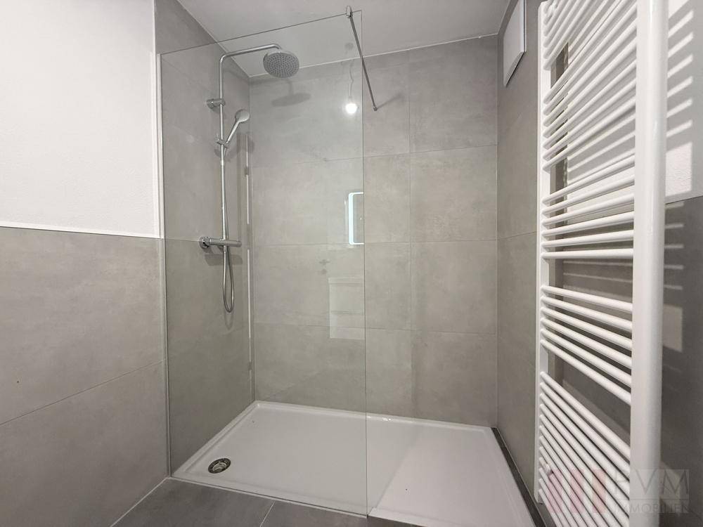 Modernes Badezimmer mit großer begehbarer Dusche und beheiztem Handtuchhalter.