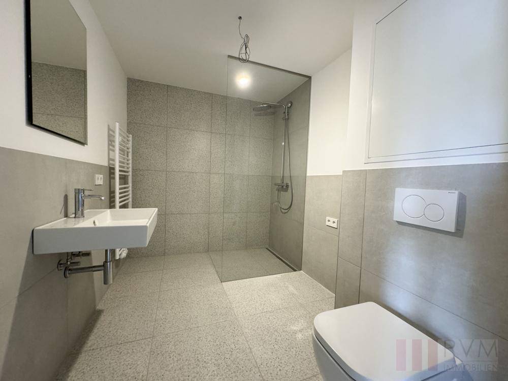 Modernes Badezimmer mit grauen Fliesen, ebenerdiger Dusche und wandhängendem WC.