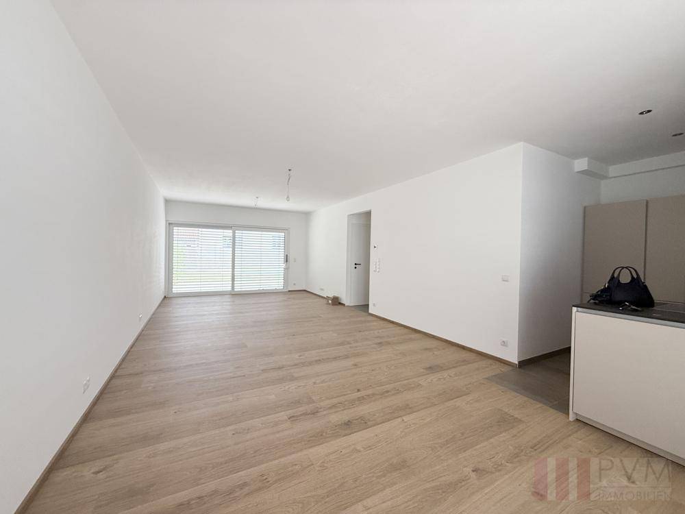 Heller, leerer Wohn-Essbereich mit Holzboden und großen Schiebetüren zur Terrasse.