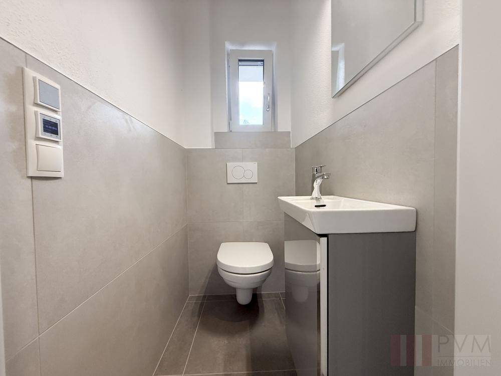 Gäste-WC mit wandhängender Toilette, modernem Waschbecken und kleinem Fenster.