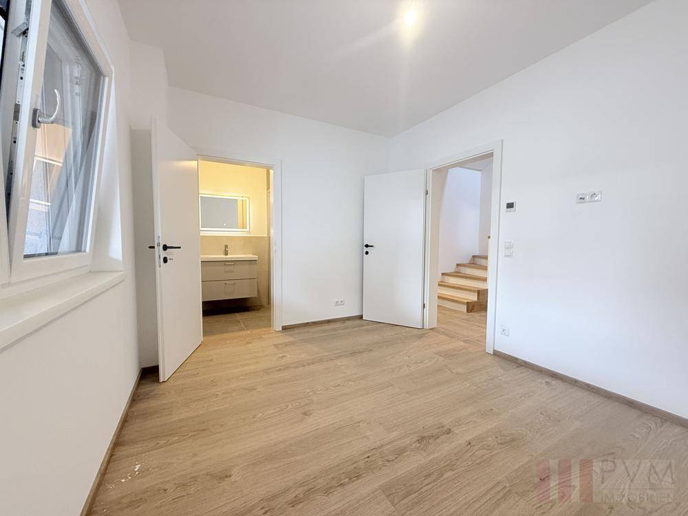 Helles Schlafzimmer mit Holzboden, Fenster und Zugang zu Bad und Treppenhaus.