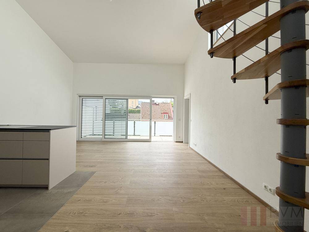 Geräumiger Wohnbereich mit offener Küche, Wendeltreppe und Zugang zum Balkon.