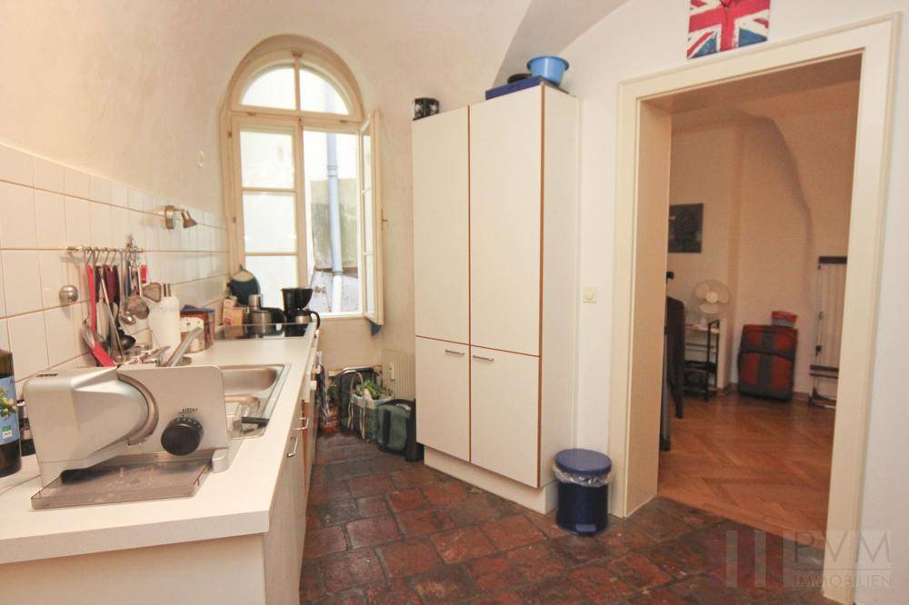 Kleine Küche mit Terrakotta-Fliesenboden, weißer Einbauküche und Rundbogenfenster.