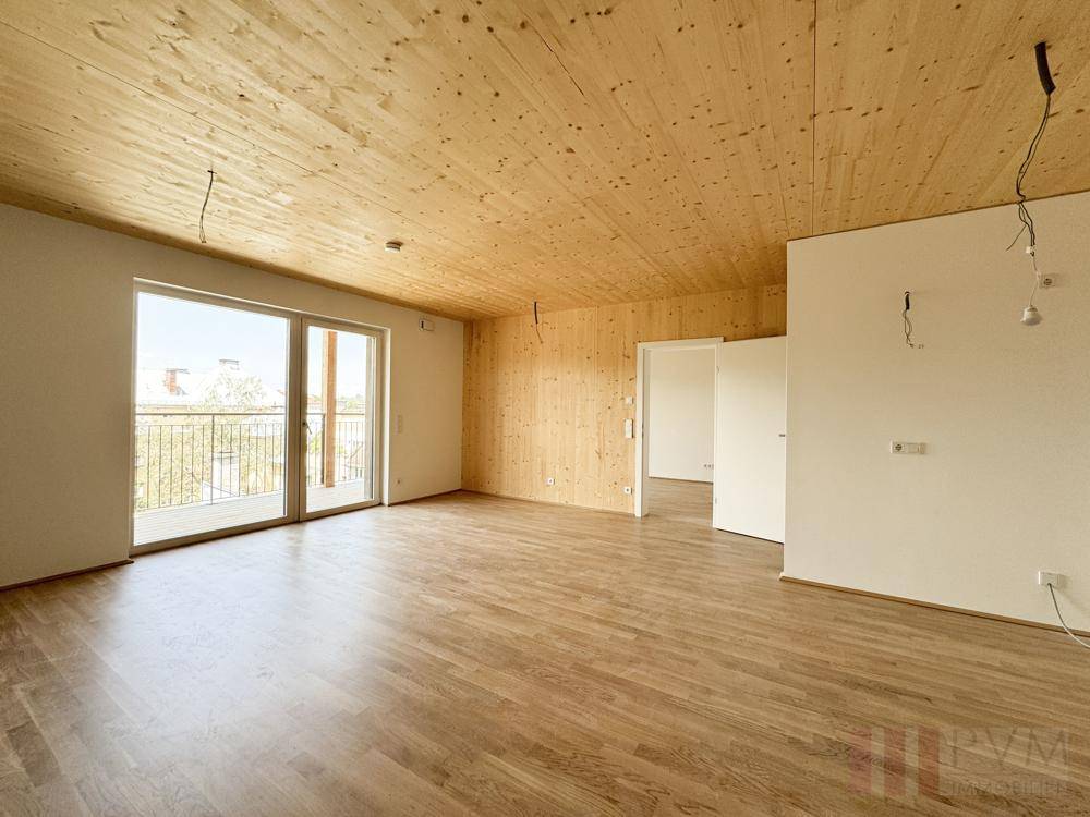 Geräumiger, unmöblierter Wohnbereich mit Holzboden, Holzdecke und Balkonzugang.