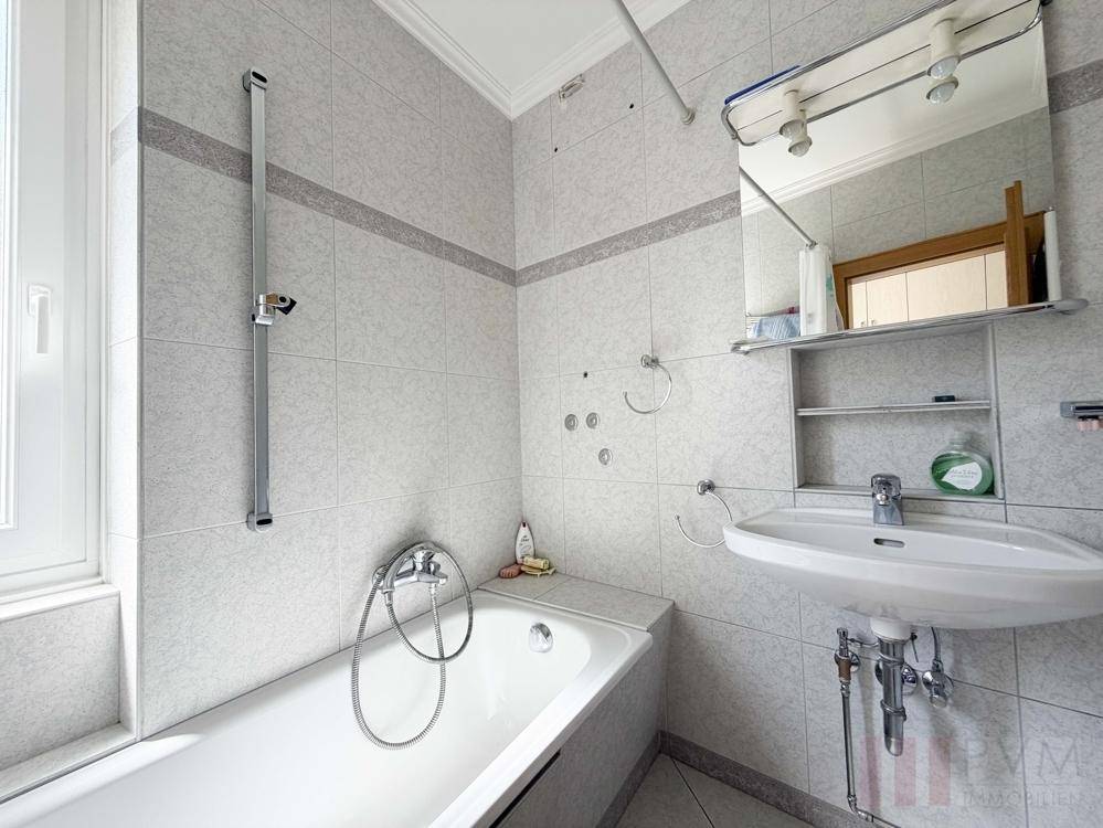 Gefliestes Badezimmer mit Badewanne, Duschfunktion, Waschbecken und Spiegelschrank.