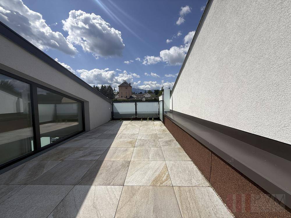 Geräumige Dachterrasse mit Fliesenboden und weitem Blick unter blauem Himmel.