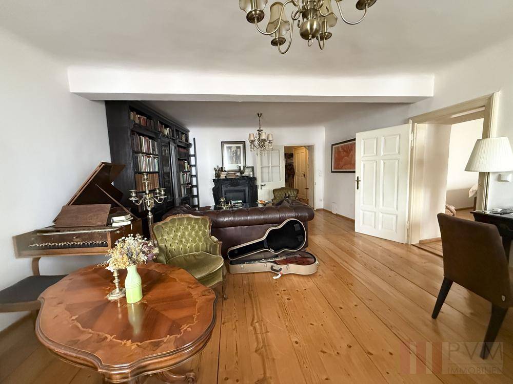 Weitläufiges Wohnzimmer mit Holzdielenboden, Flügel und antiken Möbeln.