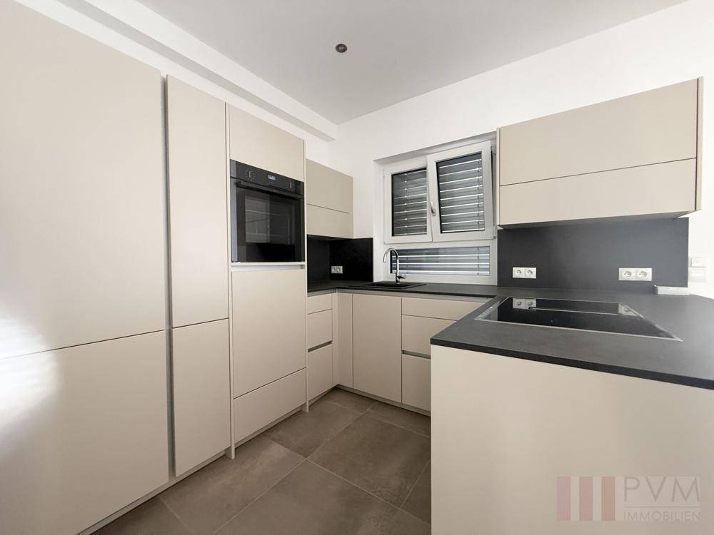 Moderne Einbauküche in hellem Beige mit dunkler Arbeitsplatte und integriertem Backofen.