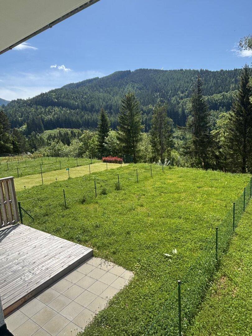 Sonniger Gartenbereich mit Holzterrasse und weitem Blick auf die grüne Berglandschaft.