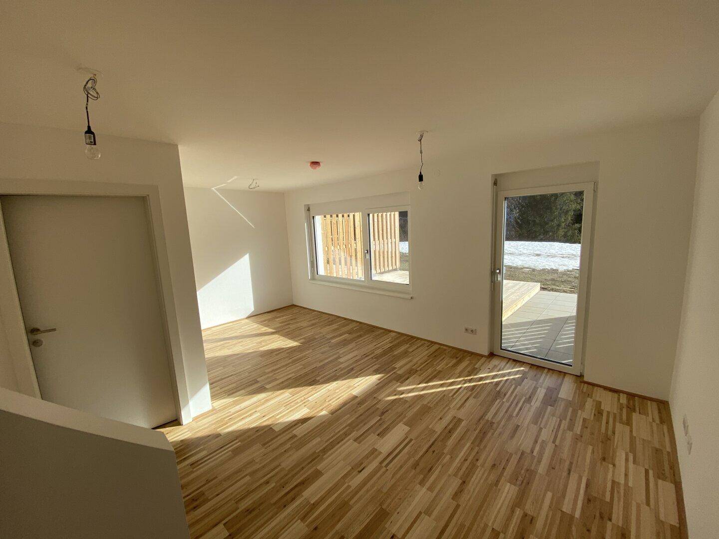 Heller Raum mit Holzboden, weißen Wänden und Zugang zu einem verschneiten Außenbereich.
