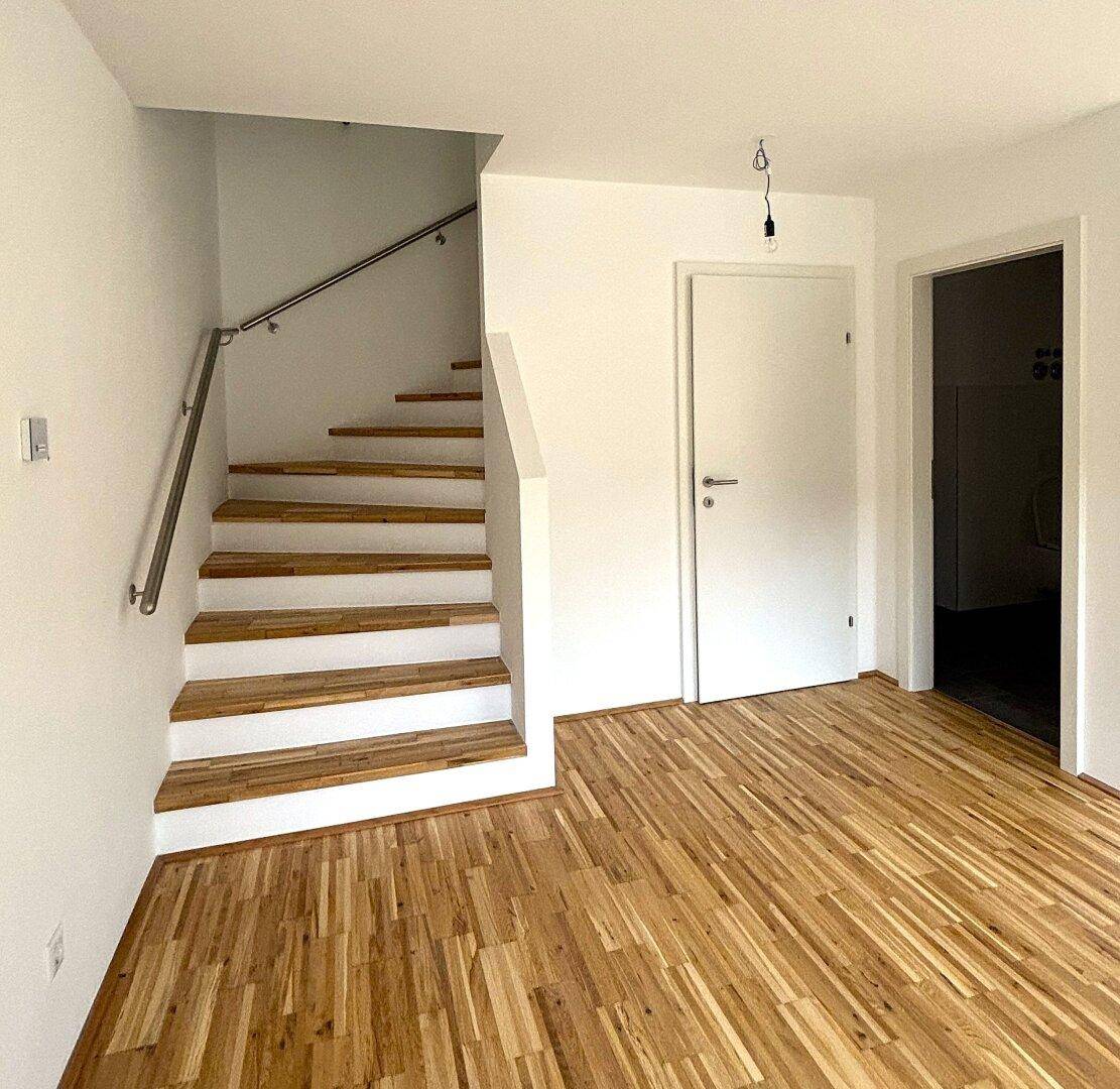 Heller Flurbereich mit Holzboden und moderner Holztreppe mit Metallgeländer.