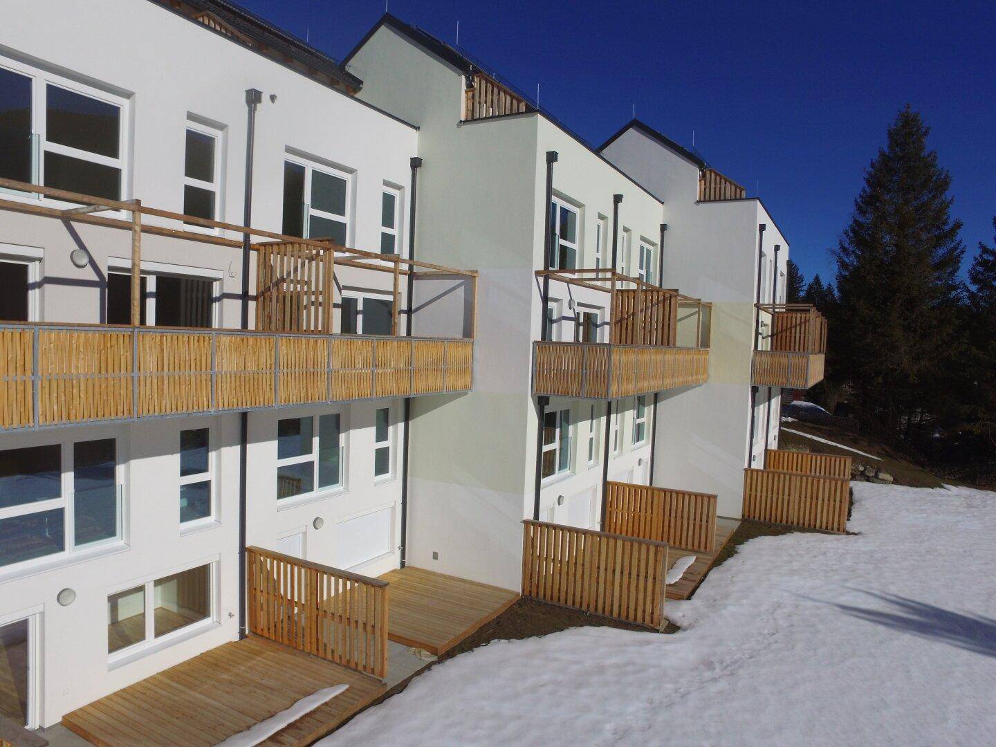 Reihe moderner Wohneinheiten mit Holzterrassen und Balkonen in verschneiter Umgebung.