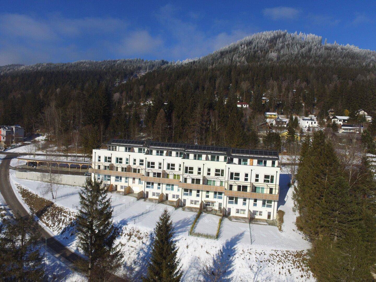 Luftaufnahme einer modernen Wohnanlage mit Solaranlagen auf dem Dach in Winterlandschaft.