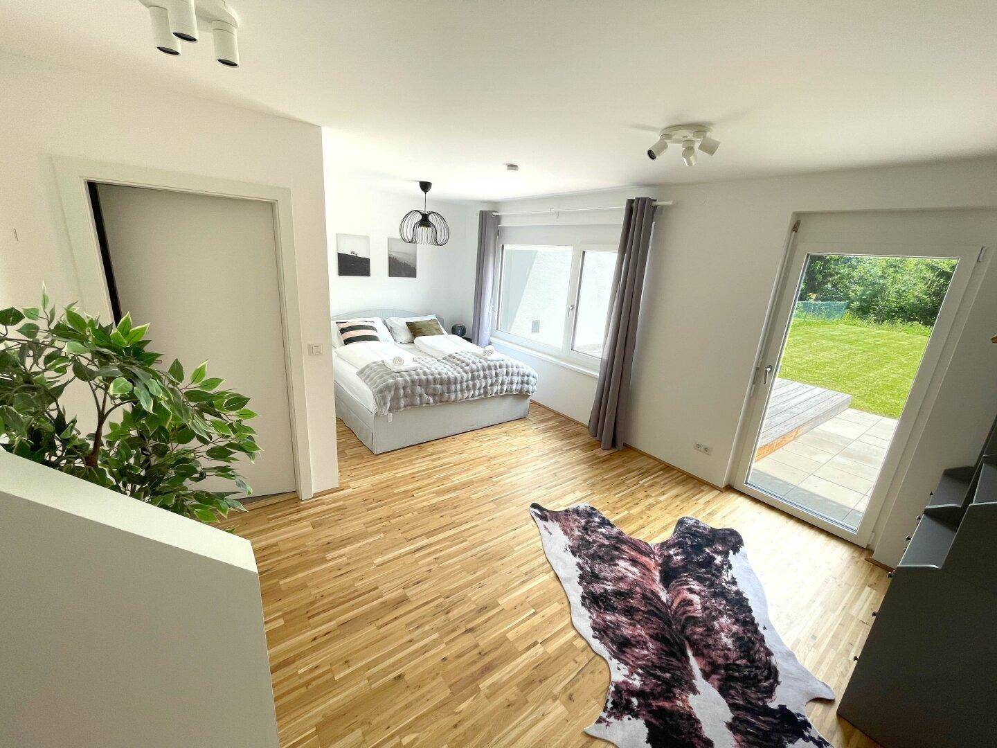Helles Schlafzimmer mit Holzboden, großem Fenster und Zugang zu einem Außenbereich.
