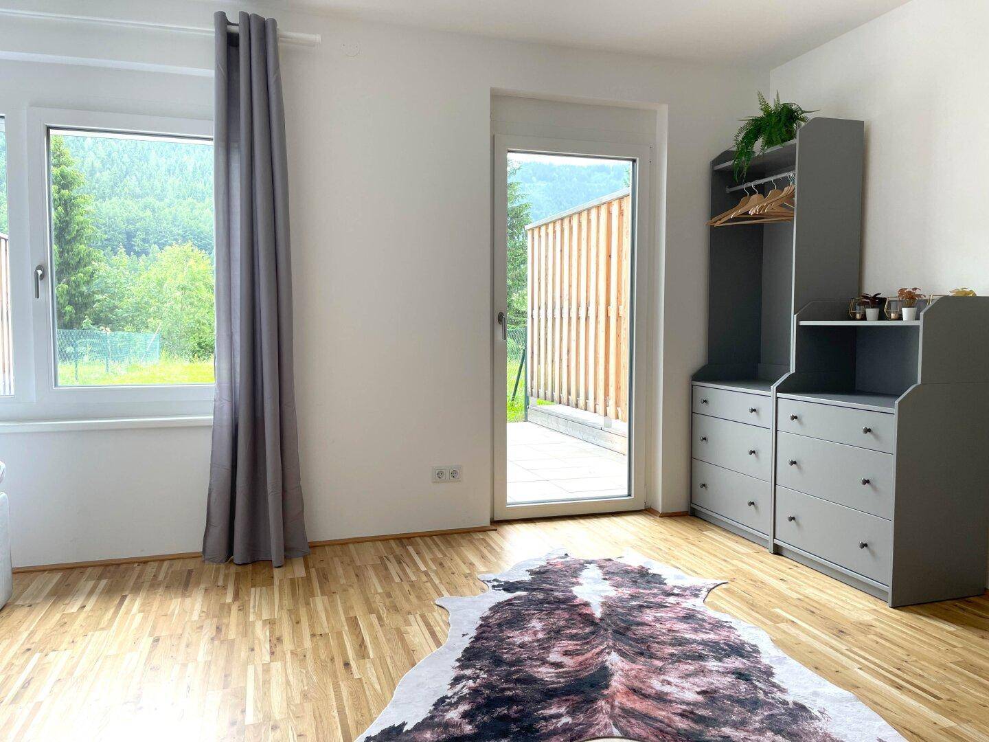 Helles Schlafzimmer mit Holzboden, grauem Schrank und Zugang zu einem Außenbereich mit grüner Aussicht.