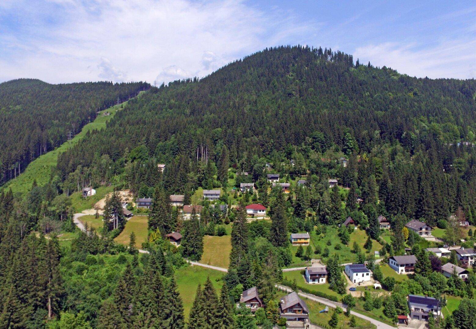 Luftaufnahme eines malerischen Bergdorfes, umgeben von dichten Wäldern und grünen Hügeln.