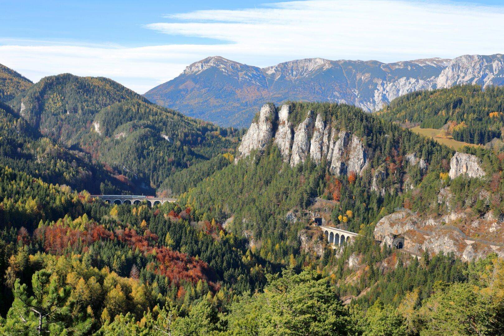 Atemberaubende Berglandschaft mit bewaldeten Hängen, Felsformationen und Brücken im Herbst.
