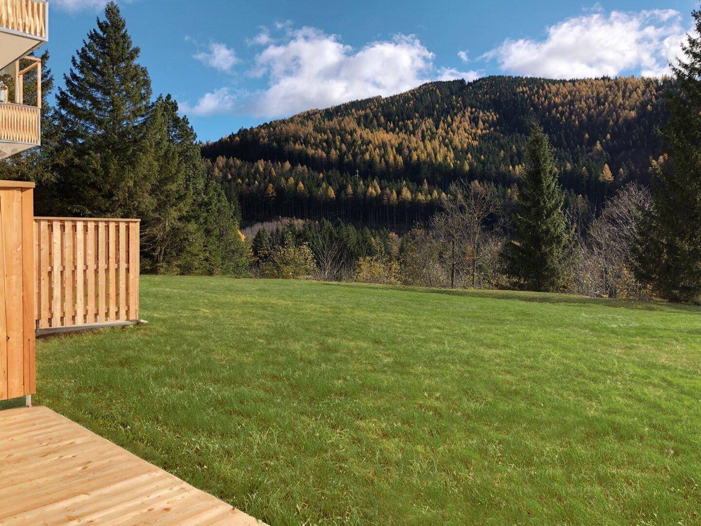 Gepflegte Rasenfläche mit Holzzaun und weitem Blick auf die herbstliche Berglandschaft.