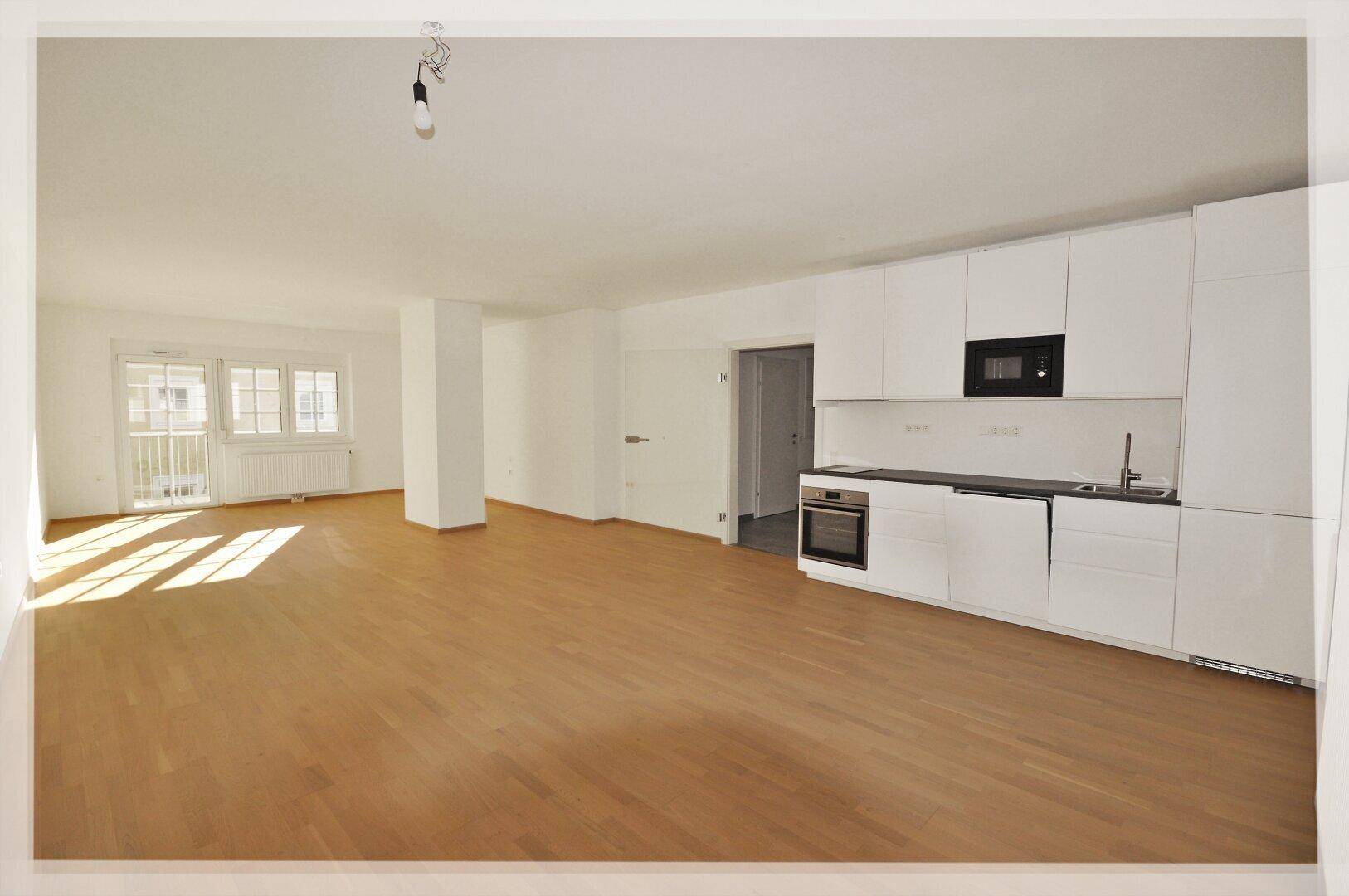 Heller, offener Wohnbereich mit integrierter moderner Küche, Parkettboden und Zugang zum Balkon.